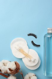 Photo of Bottle of makeup remover, cotton flowers, pads, swabs and false eyelashes on light blue background, flat lay. Space for text