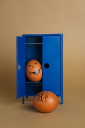 Photo of Happy egg hiding in closet and playing prank on another one against brown background