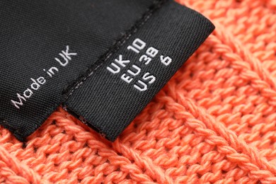 Photo of Clothing labels on knitted orange garment, closeup