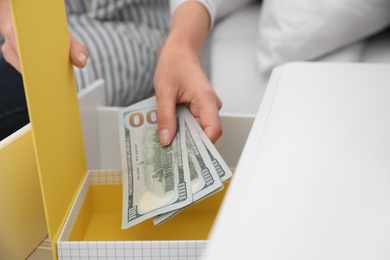 Woman hiding dollar banknotes in box at home, closeup. Money savings