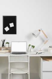 Photo of Cozy workspace with laptop, lamp and stationery on wooden desk at home