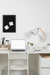 Cozy workspace with laptop, lamp and stationery on wooden desk at home