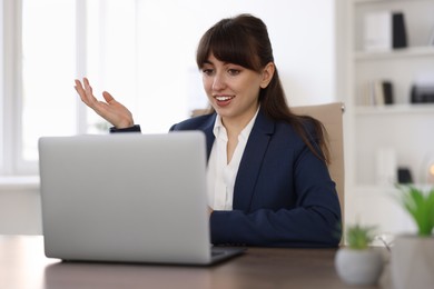 Photo of Woman using video chat during webinar at wooden table in office