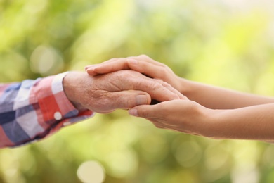 Photo of Young woman holding elderly man hand on blurred background, closeup. Help service