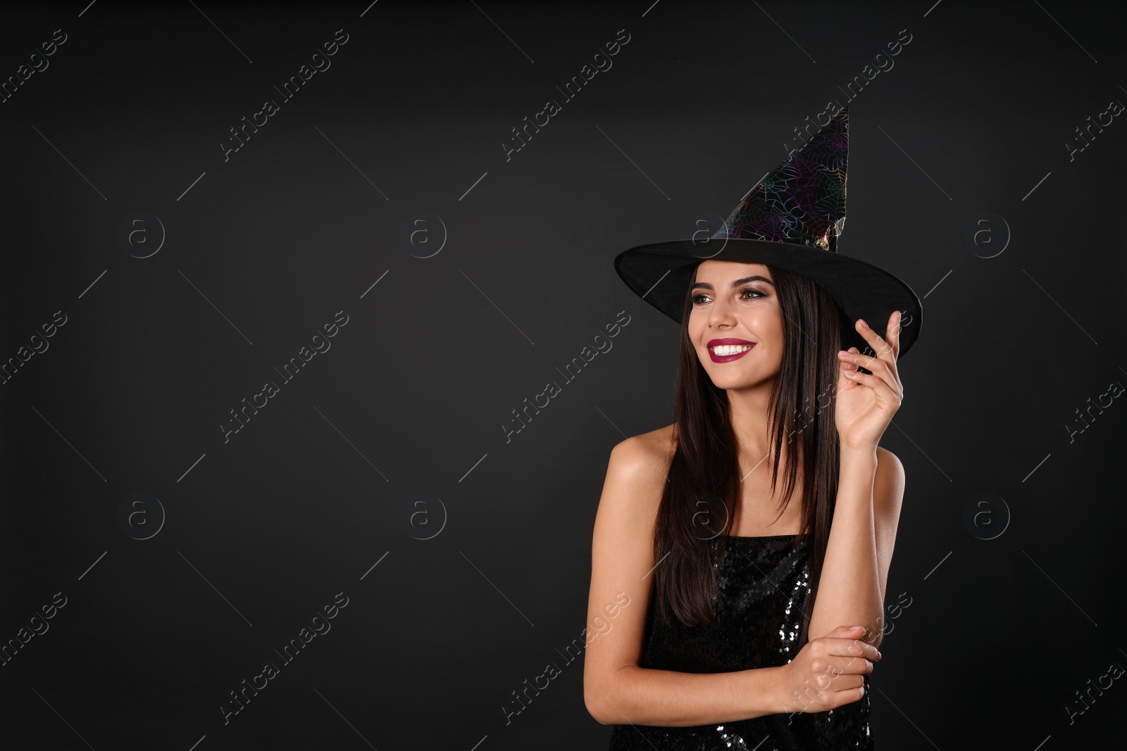 Photo of Beautiful woman wearing witch costume for Halloween party on black background, space for text