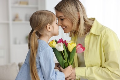 Little daughter congratulating her mom with bouquet of tulips at home. Happy Mother's Day