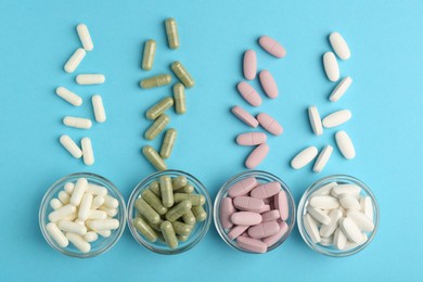 Different vitamin pills on light blue background, flat lay