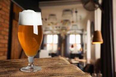 Image of Glass with fresh beer on wooden table in pub, space for text