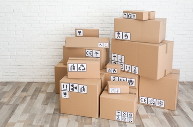 Photo of Cardboard boxes with different packaging symbols on floor near white brick wall. Parcel delivery