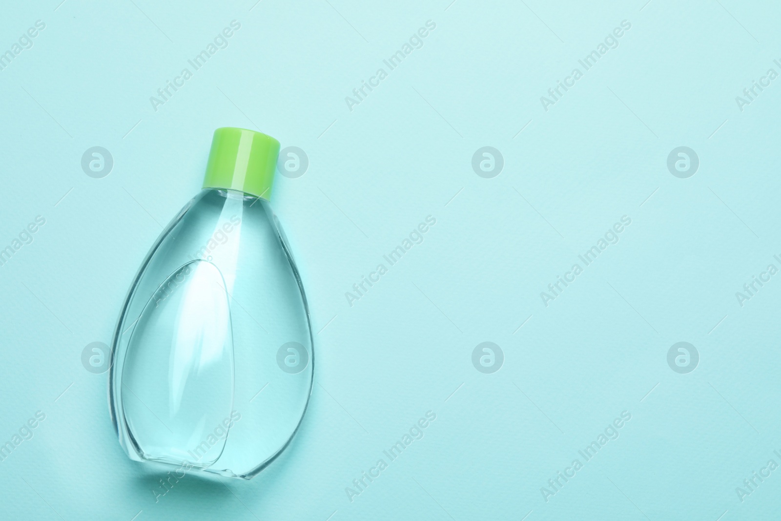Photo of Bottle of baby oil on turquoise background, top view. Space for text