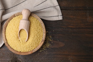 Photo of Bowl and scoop with raw couscous on wooden table, top view. Space for text