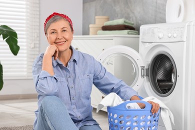 Photo of Happy housewife with laundry basket near washing machine at home