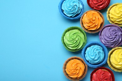 Photo of Many tasty cupcakes with bright cream on light blue background, flat lay. Space for text