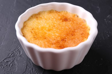 Photo of Delicious creme brulee in bowl on dark gray textured table, closeup