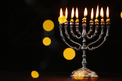 Photo of Silver menorah with burning candles against dark background and blurred festive lights, space for text. Hanukkah celebration