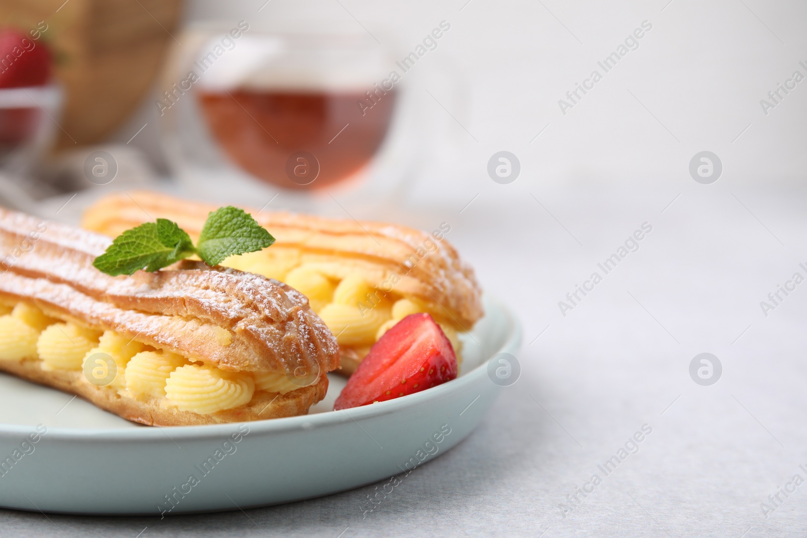 Photo of Delicious eclairs filled with cream, strawberry and mint on table, closeup. Space for text