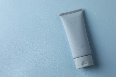 Photo of Moisturizing cream in tube on light blue background with water drops, top view. Space for text