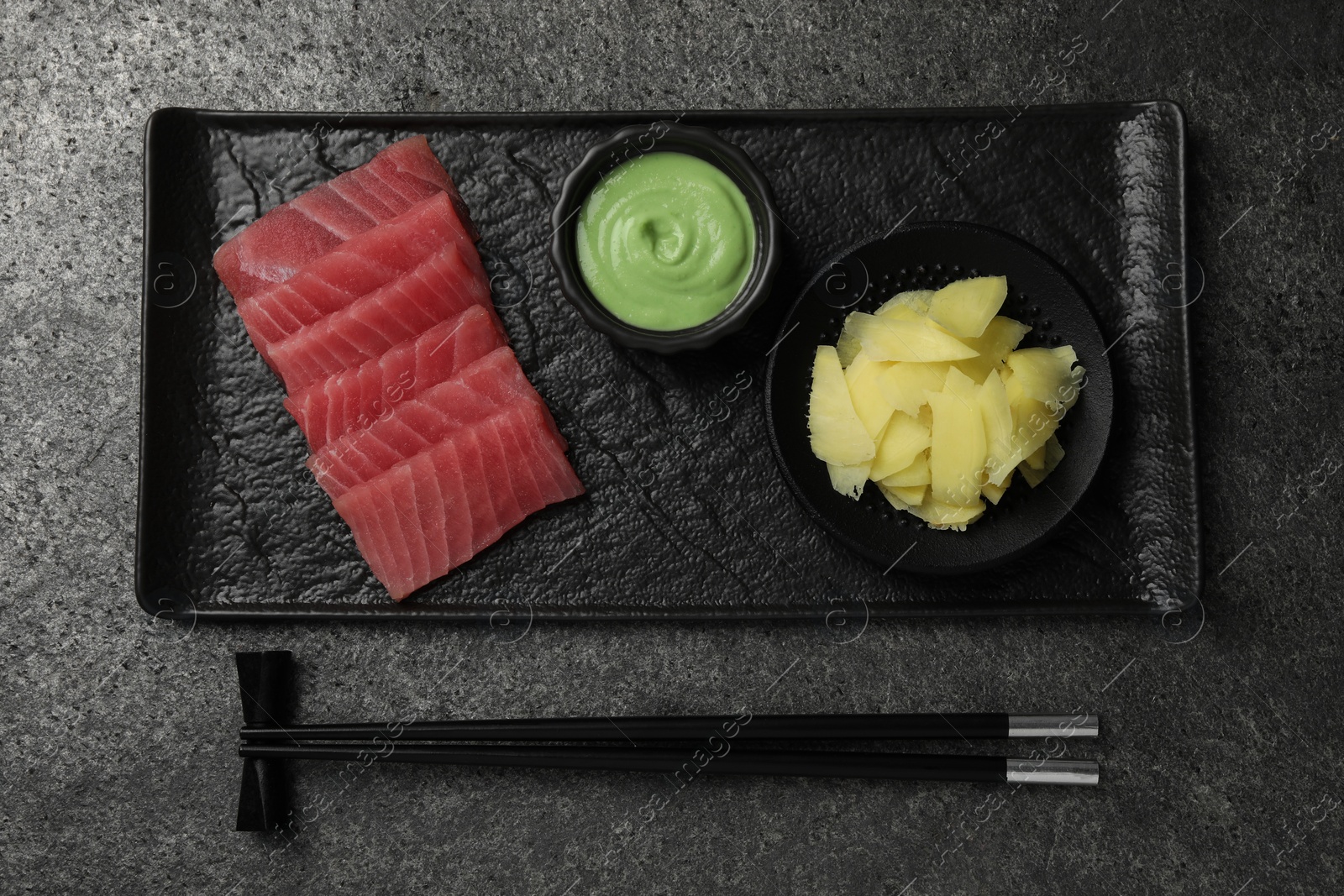 Photo of Tasty sashimi (pieces of fresh raw tuna) served with wasabi sauce and ginger slices on gray table, flat lay