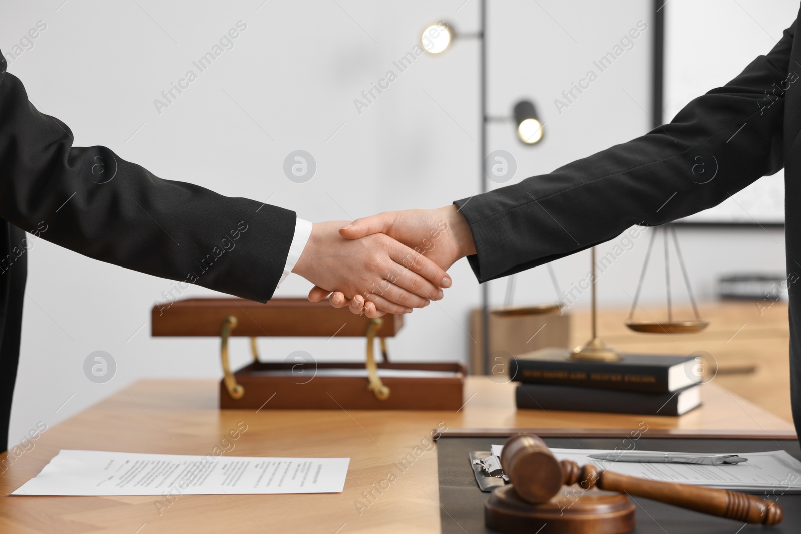 Photo of Notary shaking hands with client at wooden table in office, closeup