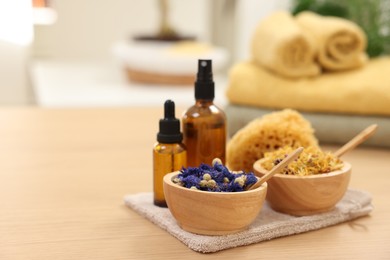Photo of Bottles of essential oils, bowls with dry flowers and natural sponge on light wooden table, space for text. Spa therapy