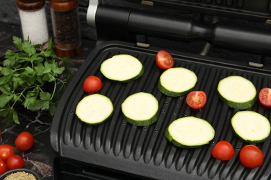 Photo of Electric grill with vegetables on black marble table, closeup