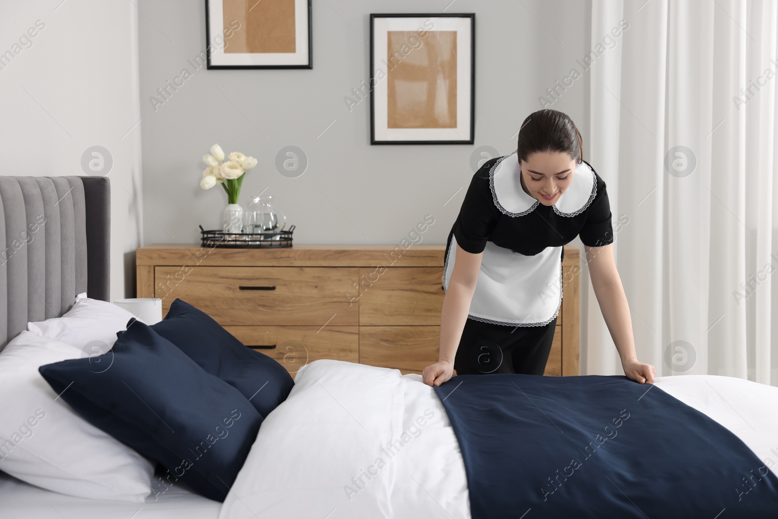 Photo of Young chambermaid making bed in hotel room