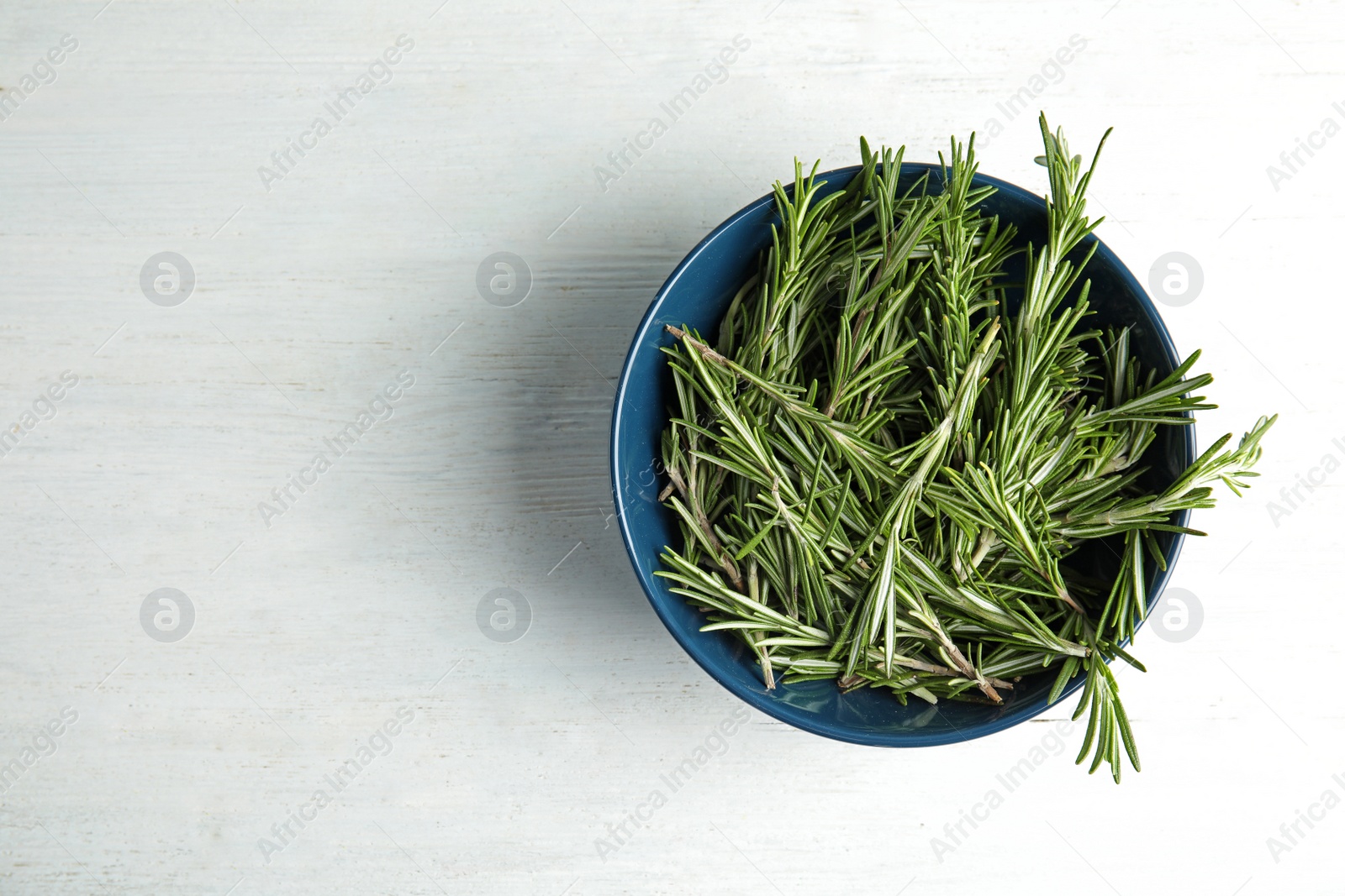 Photo of Bowl with fresh rosemary twigs on wooden table, top view. Space for text