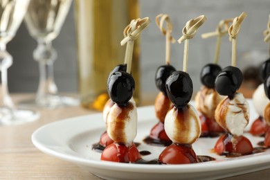 Photo of Tasty canapes with black olives, mozzarella and cherry tomatoes on light wooden table, closeup