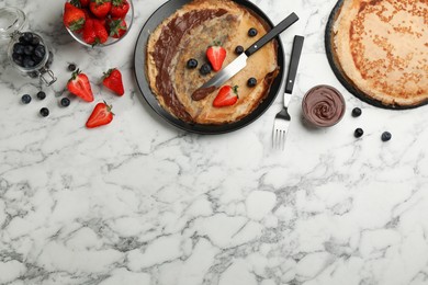 Photo of Delicious thin pancakes served with chocolate paste and berries on white marble table, flat lay. Space for text