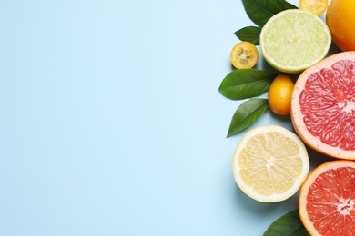 Photo of Fresh juicy citrus fruits with green leaves on light blue background, flat lay. Space for text