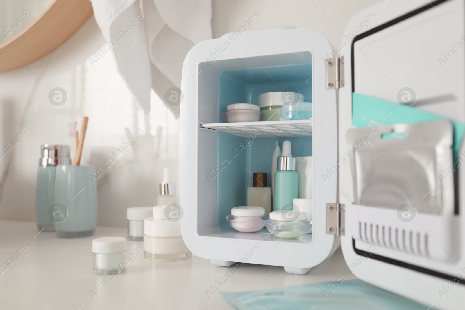 Photo of Cosmetics refrigerator and skin care products on white table indoors, closeup