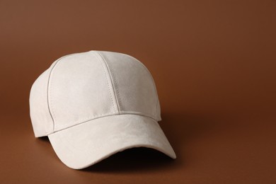 Stylish beige baseball cap on brown background. Space for text