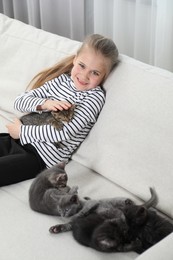 Photo of Little girl with fluffy kittens on sofa indoors