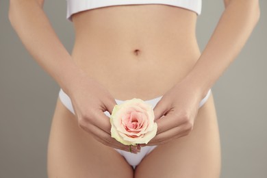 Gynecology. Woman in underwear with rose flower on grey background, closeup