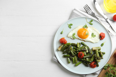 Oven baked asparagus served with fried egg on white wooden table, flat lay. Space for text