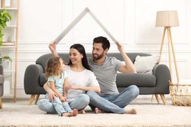 Photo of Housing concept. Happy husband holding plastic roof over his family while sitting on floor at home