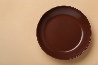 Photo of Empty brown ceramic plate on pale orange background, top view. Space for text