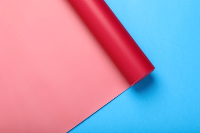 Photo of Roll of red wrapping paper on light blue background, top view. Space for text