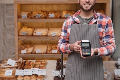 Photo of Seller holding payment terminal in bakery, closeup. Space for text