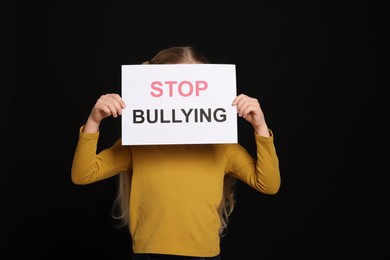 Photo of Girl holding sign with phrase Stop Bullying on black background