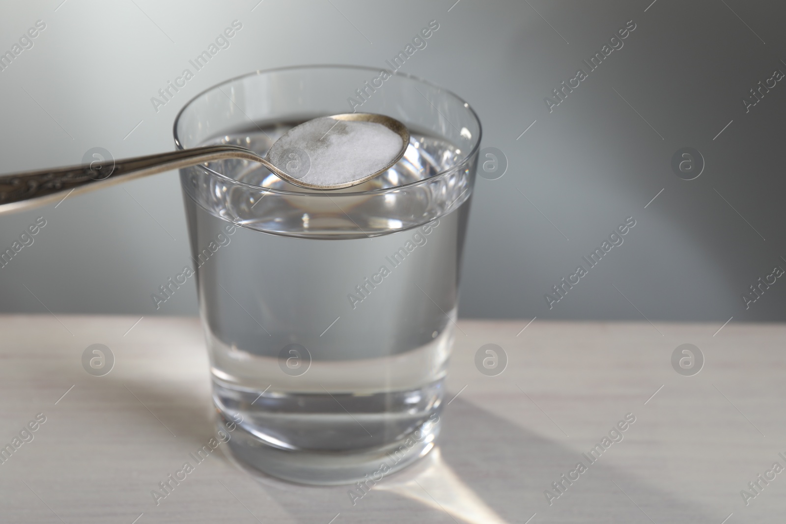 Photo of Spoon with baking soda over glass of water on table against light grey background, closeup. Space for text