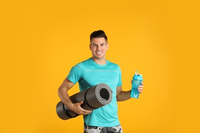 Photo of Handsome man with yoga mat and shaker on yellow background