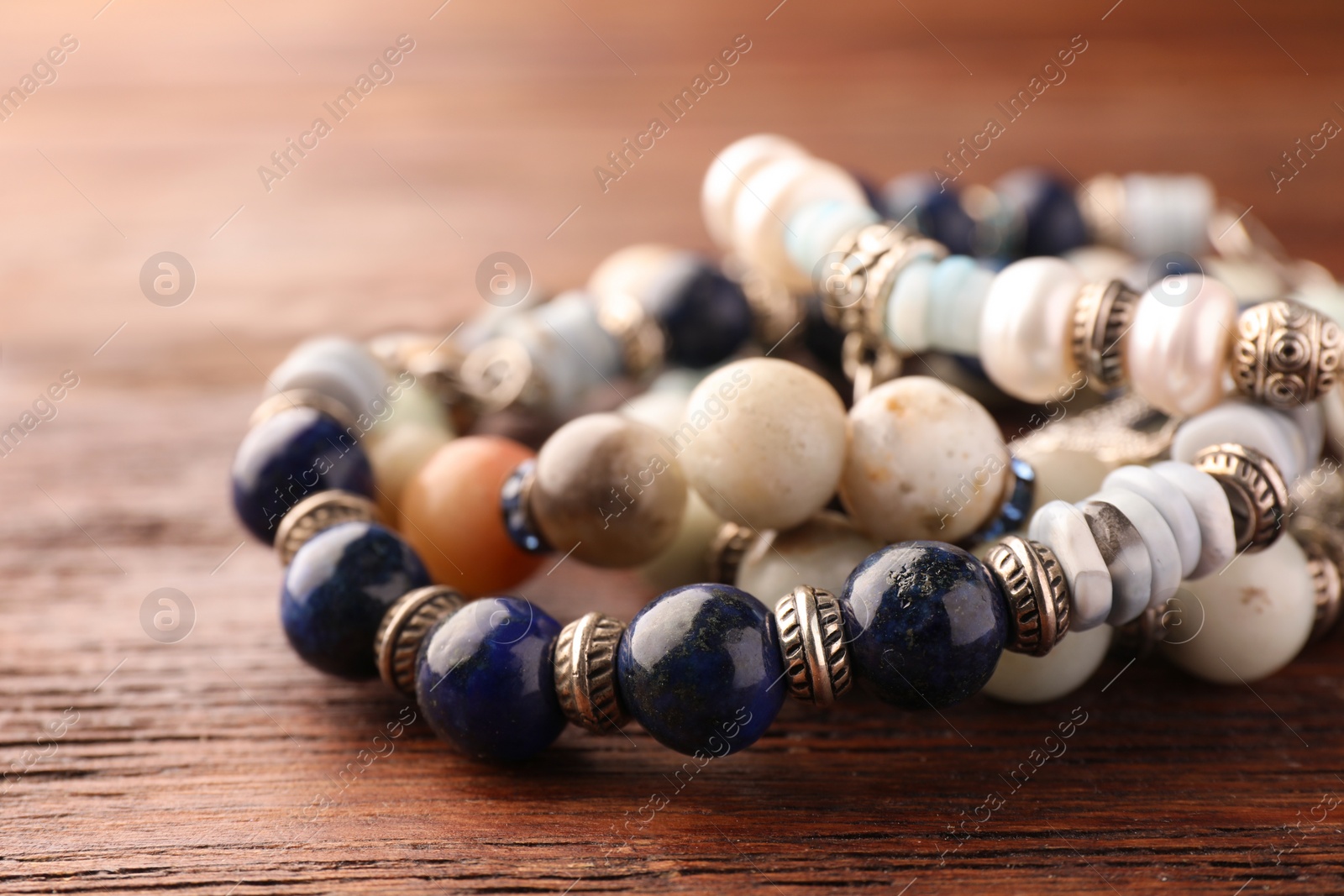 Photo of Beautiful bracelets with gemstones on wooden table, closeup