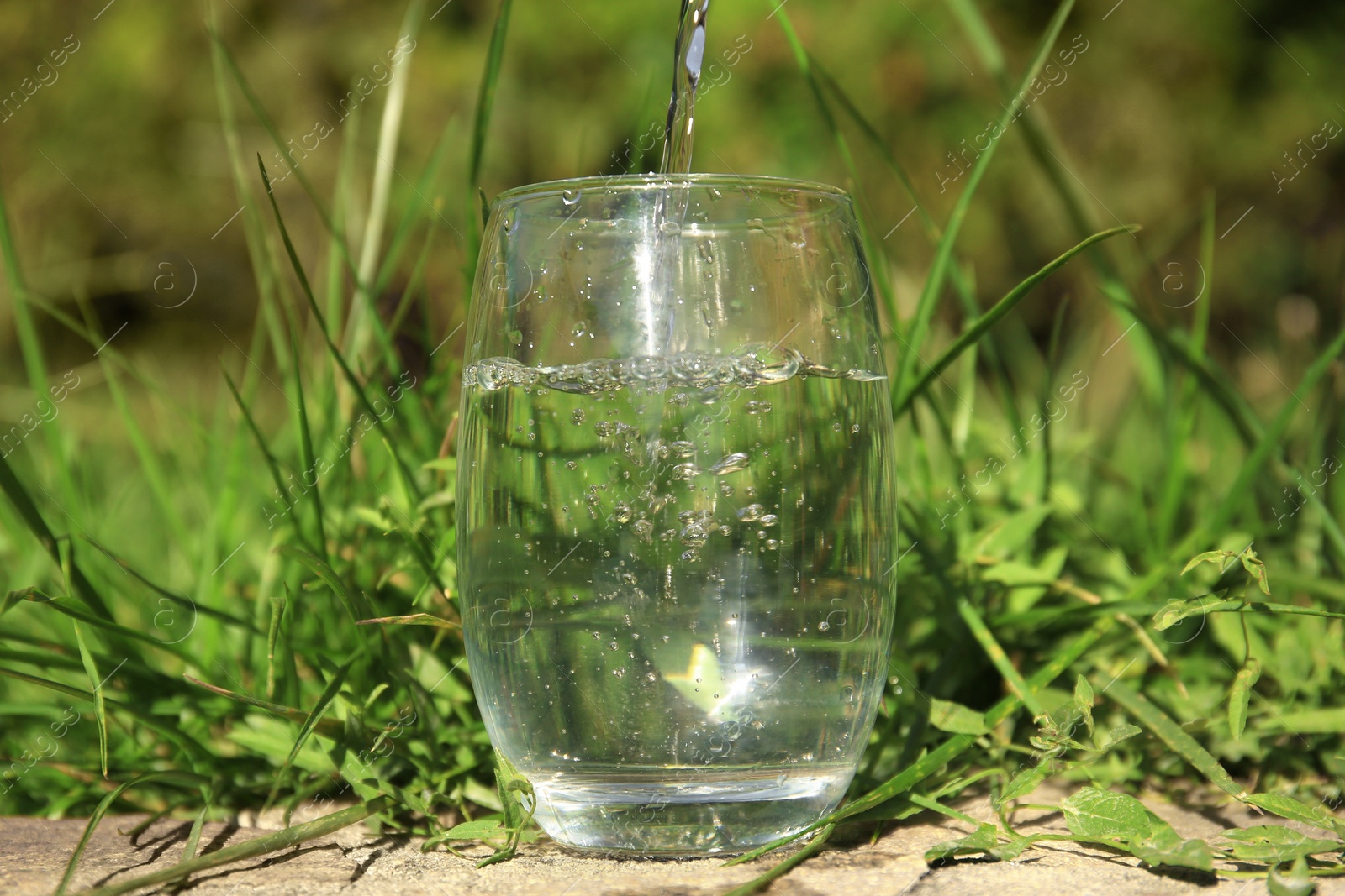 Photo of Pouring pure water into glass outdoors on sunny day
