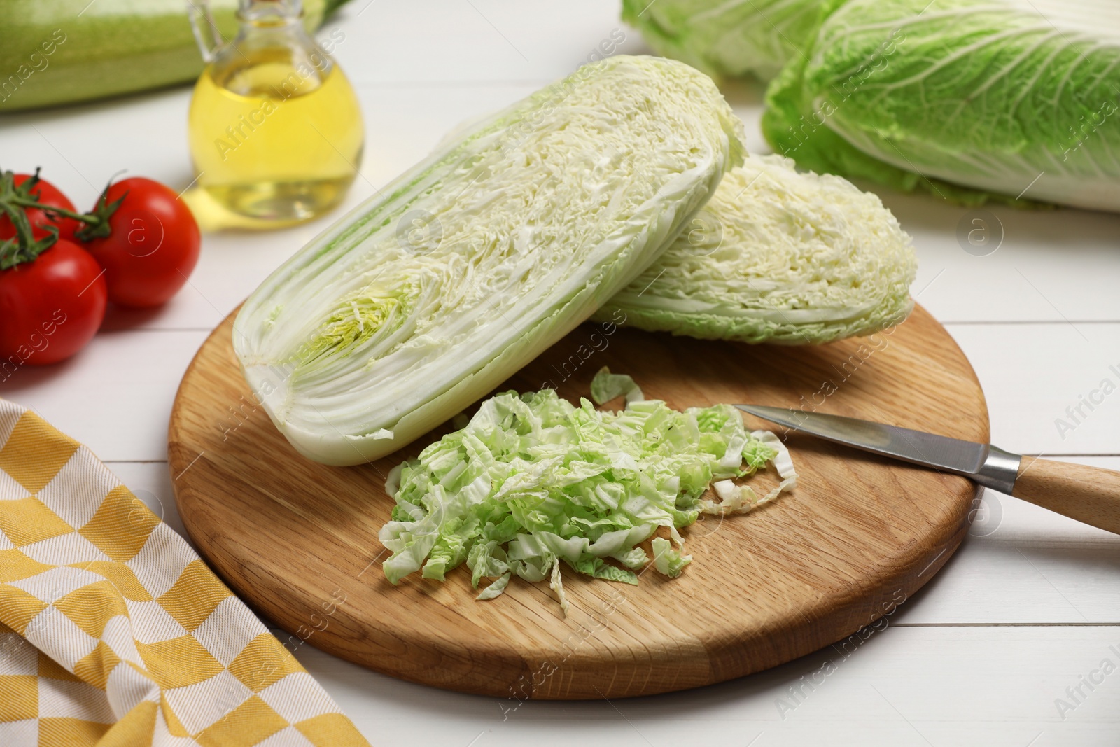 Photo of Fresh Chinese cabbages, knife, tomatoes and oil on white wooden table