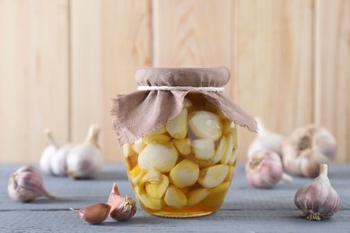 Garlic with honey in glass jar and unpeeled cloves on grey wooden table