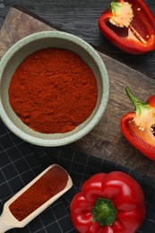 Photo of Bowl of aromatic paprika and fresh peppers on black wooden table, flat lay