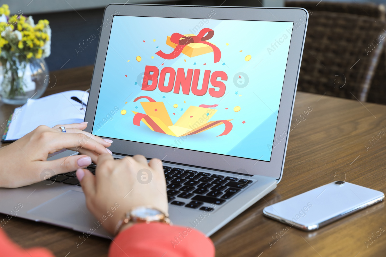 Image of Bonus gaining. Woman using laptop at wooden table indoors, closeup. Illustration of open gift box, word and confetti on device screen