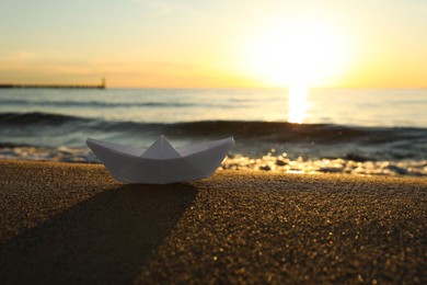 White paper boat on sand near sea at sunset, space for text