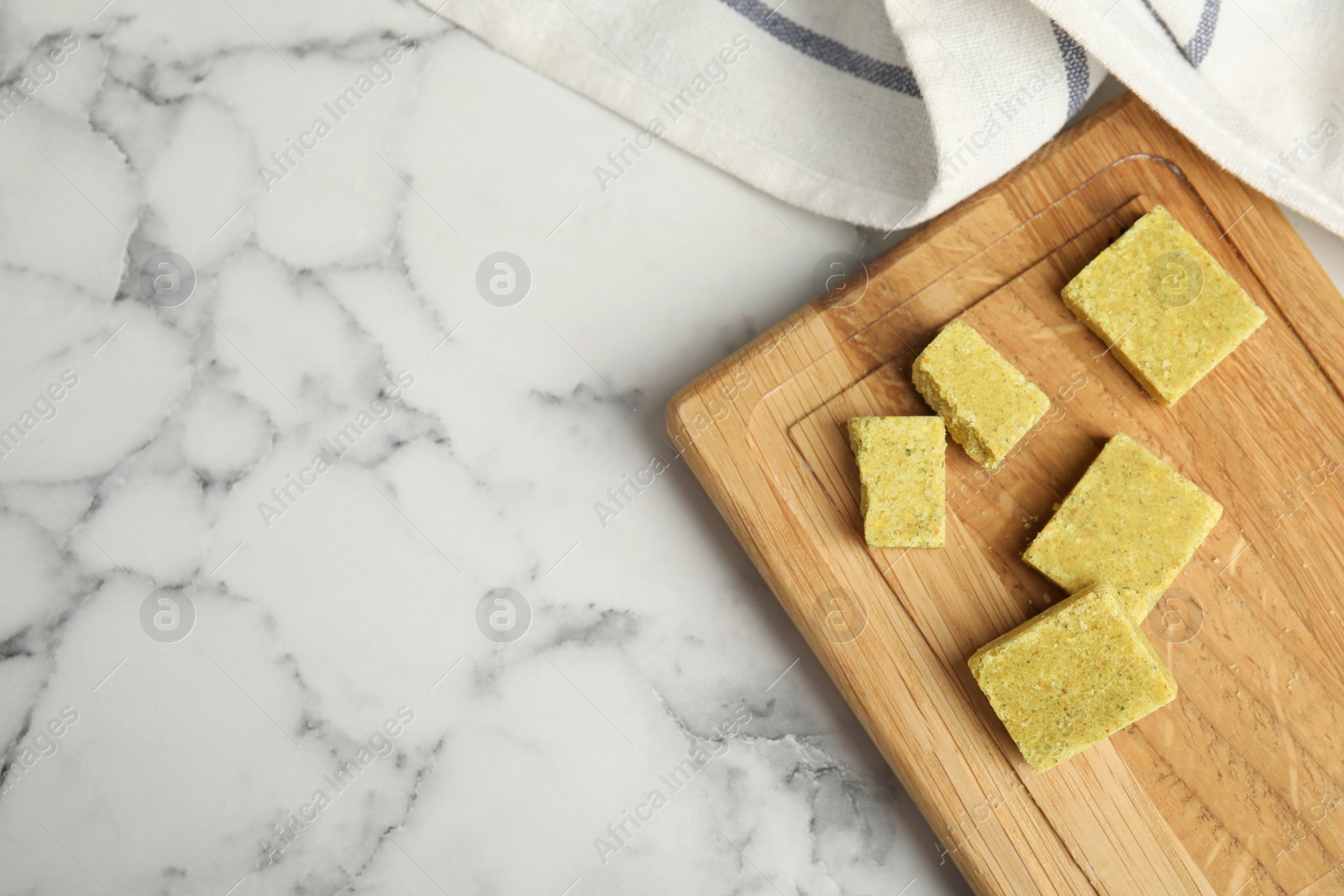 Photo of Bouillon cubes with wooden board on white marble table, top view. Space for text